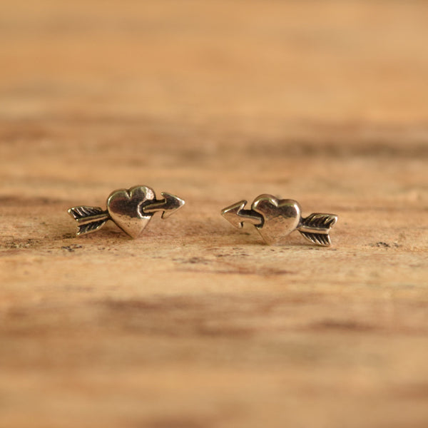 heart with arrows through stud earrings on wood background