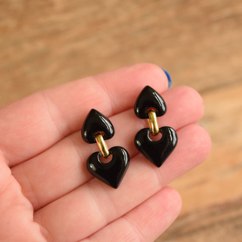 Black heart-shaped earrings held in a hand against a wooden background