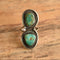 A sterling silver ring with two turquoise cabochon stones, displayed on a rustic wooden surface.