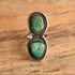 A sterling silver ring with two turquoise cabochon stones, displayed on a rustic wooden surface.