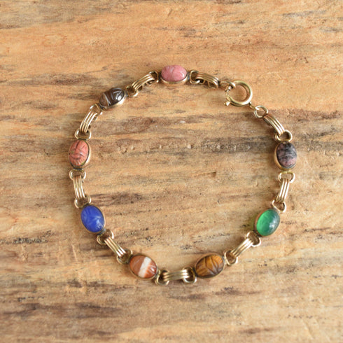 Gold filled bracelet featuring 8 gemstones carved into scarab beetles on a wooden background.