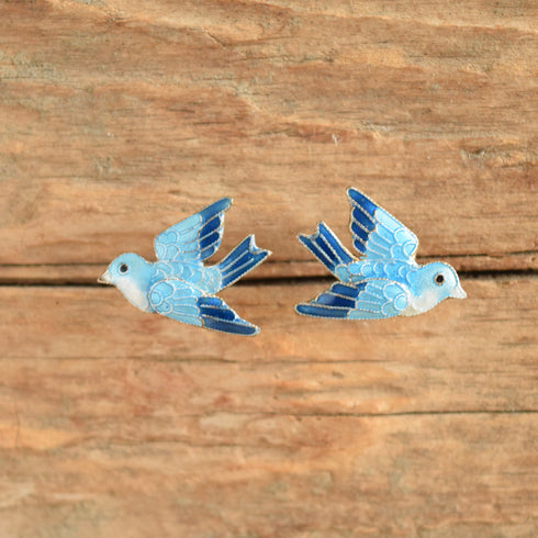 A pair of blue and white bird-shaped earrings displayed on a rustic, textured wooden background.