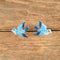 A pair of blue and white bird-shaped earrings displayed on a rustic, textured wooden background.