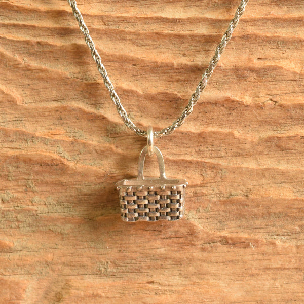 A silver necklace with a small pbasket shaped pendant, displayed against a rustic wooden background.