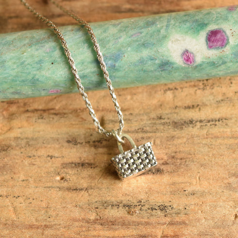 Sterling silver basket shaped pendant necklace on a wooden background with gemstone display.