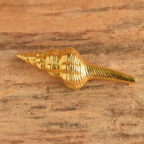 A gold toned spiral shell shaped vintage brooch on woodbackground.