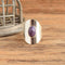 A silver-toned ring with a central oval purple gemstone, displayed on a rustic wooden surface next to a small metal basket.