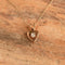 A delicate gold necklace with a heart-shaped pendant featuring a small clear gemstone, displayed on a textured brown wooden surface.
