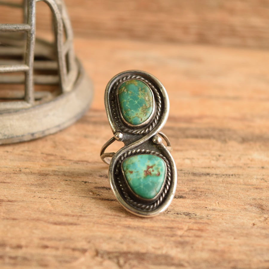 A sterling silver and turquoise ring on a wooden background with metal object in backdrop.
