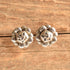 A pair of silver-toned flower shaped stud earrings resting on a rustic, textured wooden surface.