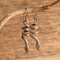 A pair of silver snake dangle earrings hanging from a natural branch against a rustic wooden background.