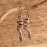 A pair of silver snake dangle earrings hanging from a natural branch against a rustic wooden background.