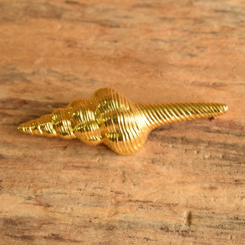 A vintage gold toned spiral seashell brooch on a wooden background