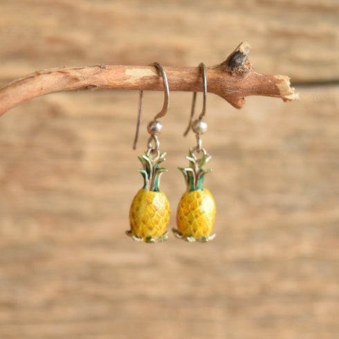 Pineapple shaped dangle enamel vintage earrings hanging on a twig. Wood backgroud.
