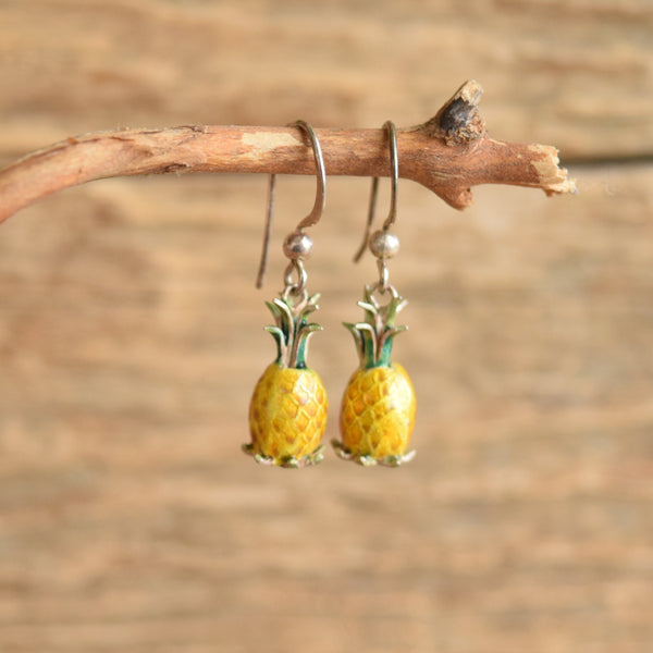 Pineapple shaped dangle enamel vintage earrings hanging on a twig. Wood backgroud.