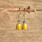 Pineapple shaped dangle enamel vintage earrings hanging on a twig. Wood backgroud.