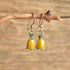 Pineapple shaped dangle enamel vintage earrings hanging on a twig. Wood backgroud.