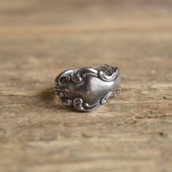 A silver vintage spoon ring with a decorative design, displayed on a wooden surface.