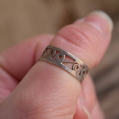 A close-up image of a person's hand showing a sterling silver swirl band ring on their finger.