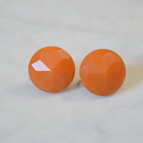 Faceted Orange bakelite screwback earrings on a white background.