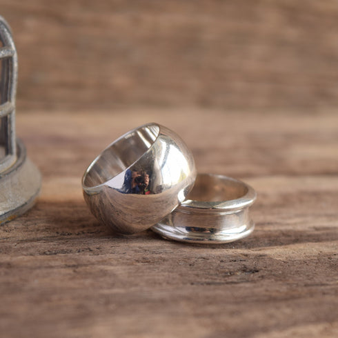 Two vintage sterling silver band rings on a wooden surface, one with a wide dome and the other with a concave band.