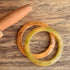 Two Bakelite flying saucer bangle bracelets in brown and green colors, displayed on a wooden surface.